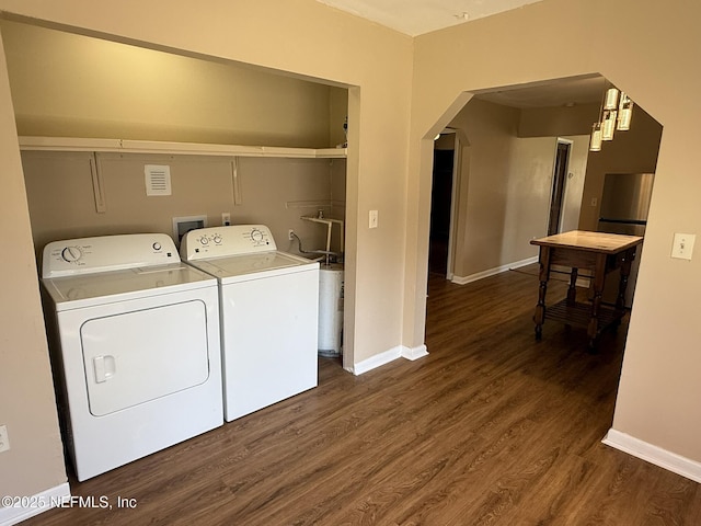 laundry room featuring dark wood finished floors, arched walkways, baseboards, laundry area, and washing machine and clothes dryer