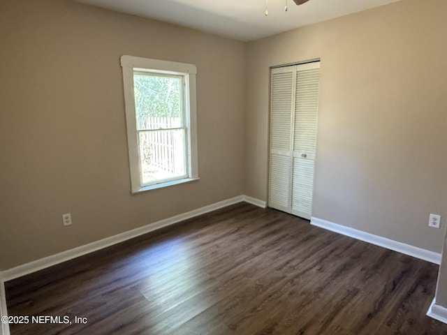 unfurnished bedroom with a closet, dark wood-style floors, and baseboards