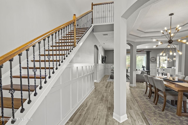 stairway featuring wood finished floors, arched walkways, a textured ceiling, a decorative wall, and a chandelier