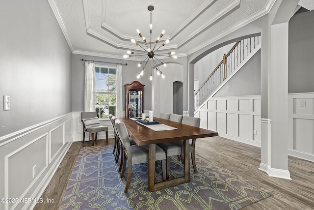 dining area featuring wood finished floors, an inviting chandelier, arched walkways, stairs, and a raised ceiling