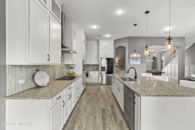 kitchen with light wood-style flooring, a sink, appliances with stainless steel finishes, wall chimney exhaust hood, and tasteful backsplash