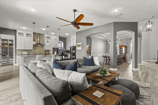 living room with visible vents, arched walkways, light wood-style floors, and a ceiling fan