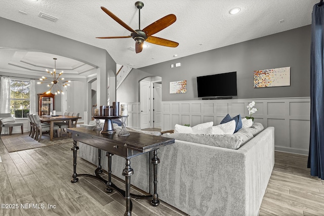 living area with a tray ceiling, a decorative wall, light wood-style floors, and arched walkways