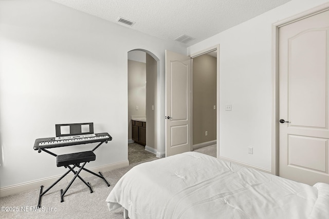 bedroom with visible vents, a textured ceiling, arched walkways, baseboards, and light colored carpet