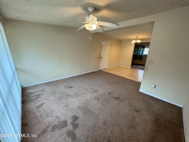 tiled empty room featuring ceiling fan with notable chandelier, carpet, baseboards, and a textured ceiling