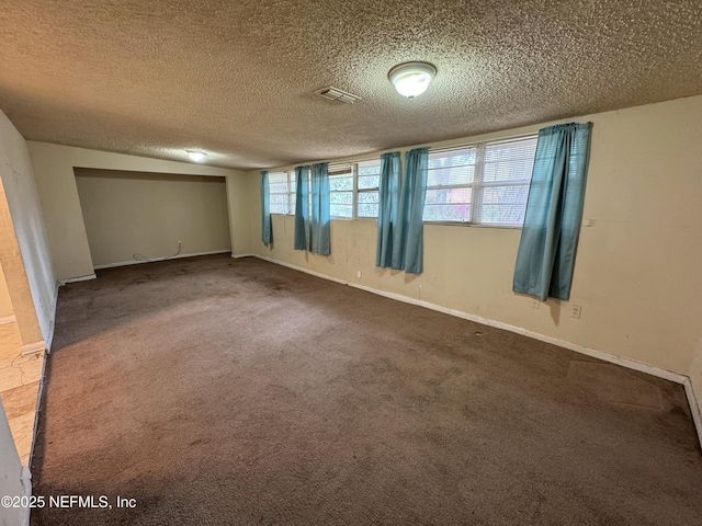 basement featuring baseboards, visible vents, carpet floors, and a textured ceiling