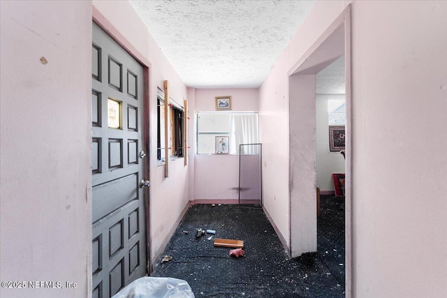 hall featuring a textured ceiling and baseboards