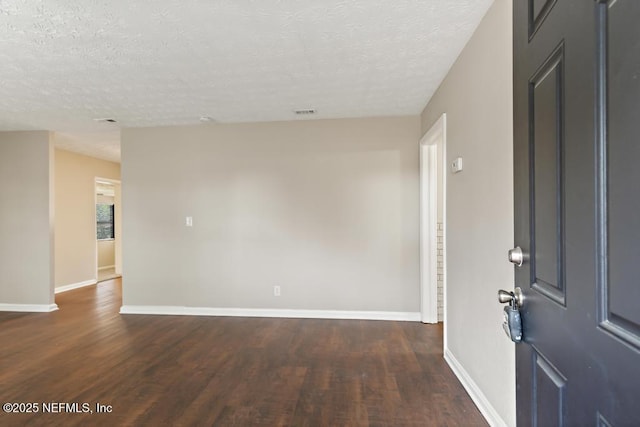 empty room featuring baseboards, a textured ceiling, and dark wood finished floors