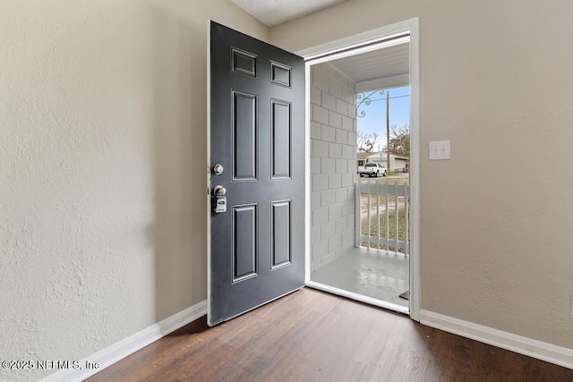 foyer entrance featuring baseboards, wood finished floors, and a textured wall