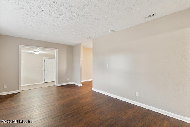 unfurnished room featuring visible vents, baseboards, dark wood-type flooring, and a textured ceiling