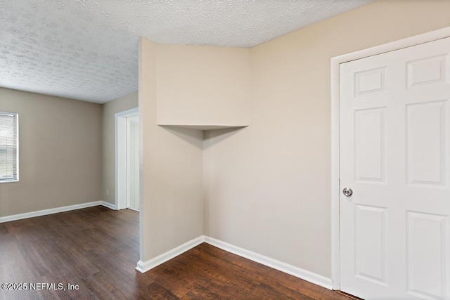 unfurnished room with baseboards, dark wood-style flooring, and a textured ceiling