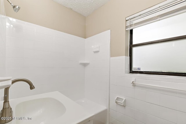 bathroom with a sink, a textured ceiling, shower / tub combination, tile walls, and wainscoting