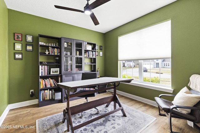 office area with light wood-style flooring, a ceiling fan, and baseboards