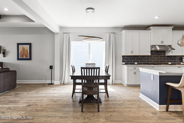 kitchen featuring under cabinet range hood, light wood-type flooring, stovetop, decorative backsplash, and white cabinetry