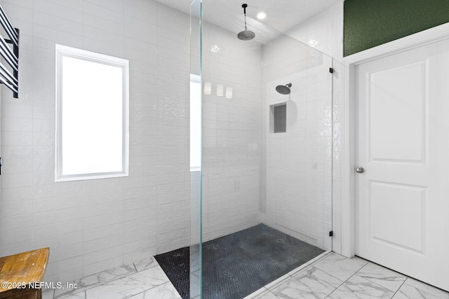 bathroom with marble finish floor and a tile shower