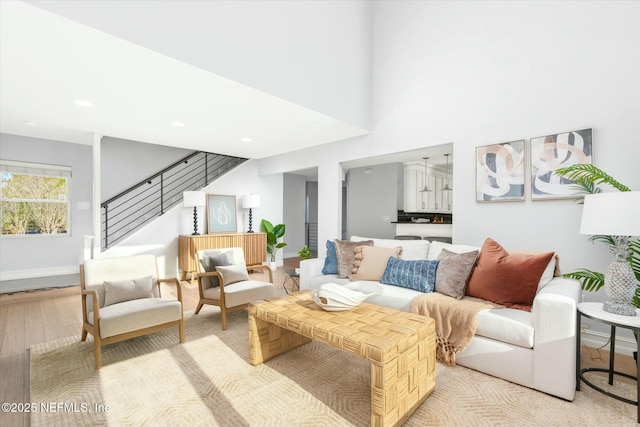 living area with a high ceiling, stairway, baseboards, and light wood-type flooring