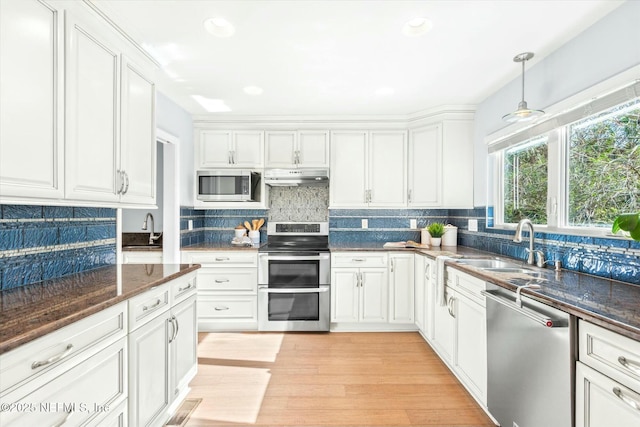 kitchen featuring light wood finished floors, under cabinet range hood, white cabinets, stainless steel appliances, and a sink