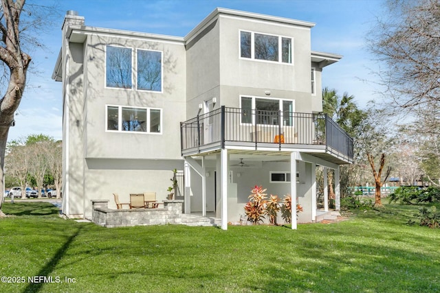 rear view of property featuring stucco siding, a lawn, a balcony, a patio area, and a ceiling fan