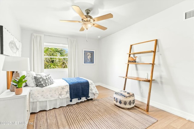 bedroom with visible vents, light wood-style flooring, a ceiling fan, and baseboards