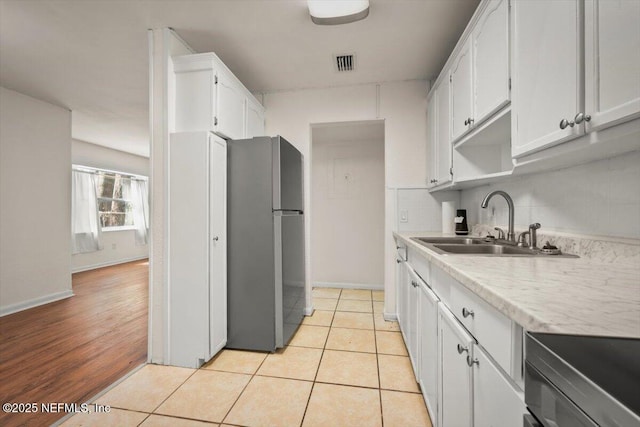 kitchen with tasteful backsplash, visible vents, light countertops, white cabinets, and a sink