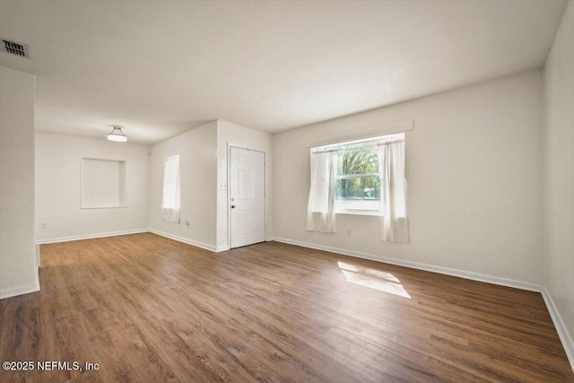 unfurnished room featuring wood finished floors, visible vents, and baseboards