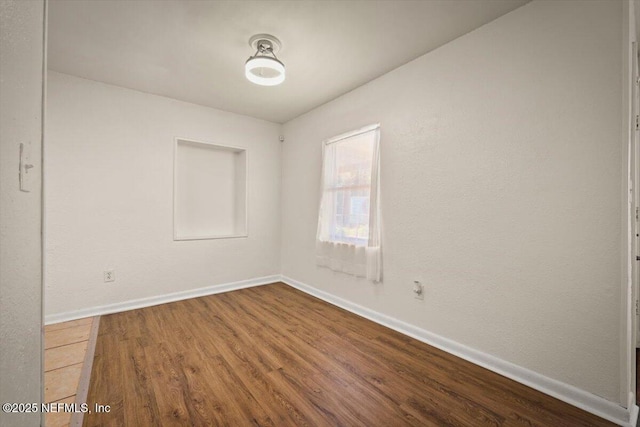 spare room with baseboards and wood finished floors