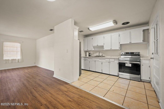 kitchen featuring light wood-style flooring, light countertops, stainless steel range with electric stovetop, white cabinetry, and open floor plan