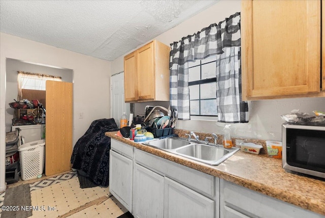 kitchen featuring a sink, stainless steel microwave, a textured ceiling, light countertops, and light floors