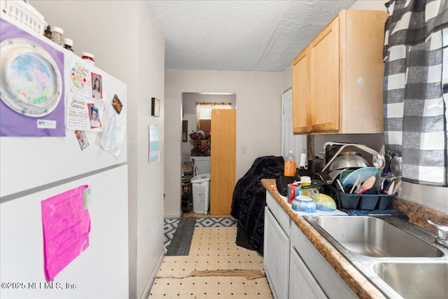 kitchen with light brown cabinets, light floors, freestanding refrigerator, a textured ceiling, and a sink