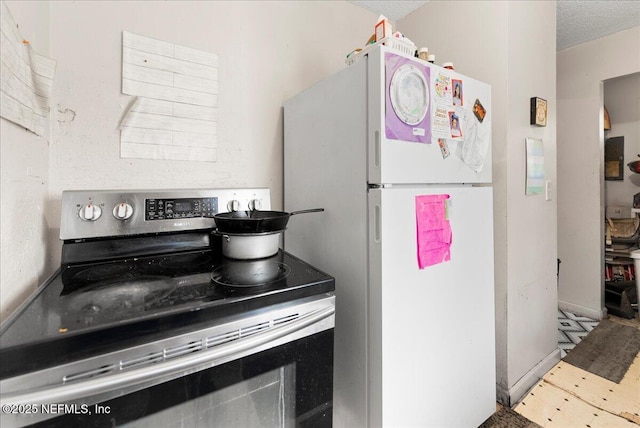 kitchen with stainless steel electric range, a textured ceiling, and freestanding refrigerator