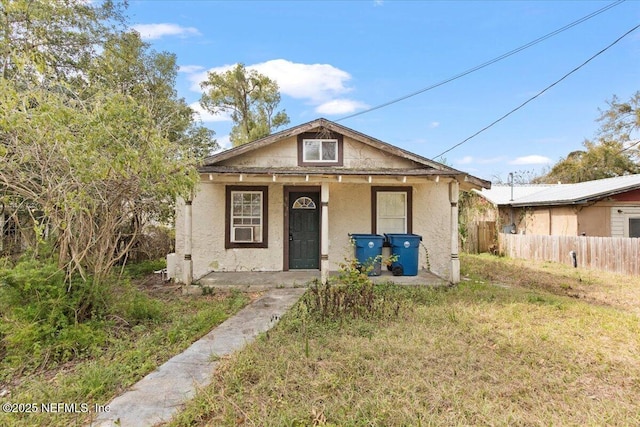 bungalow with stucco siding, covered porch, and fence