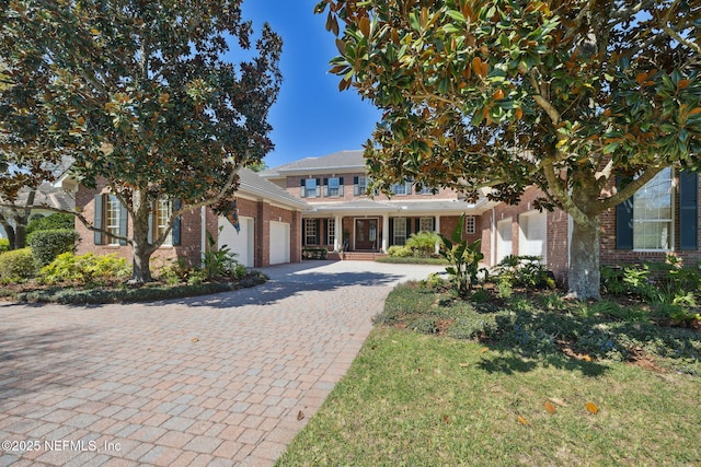 view of property hidden behind natural elements featuring decorative driveway, brick siding, and an attached garage