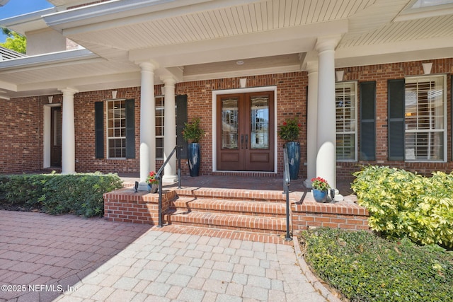 view of exterior entry featuring french doors, brick siding, and a porch