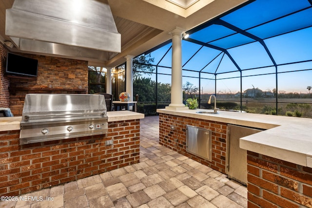 patio terrace at dusk with a lanai, grilling area, exterior kitchen, and a sink
