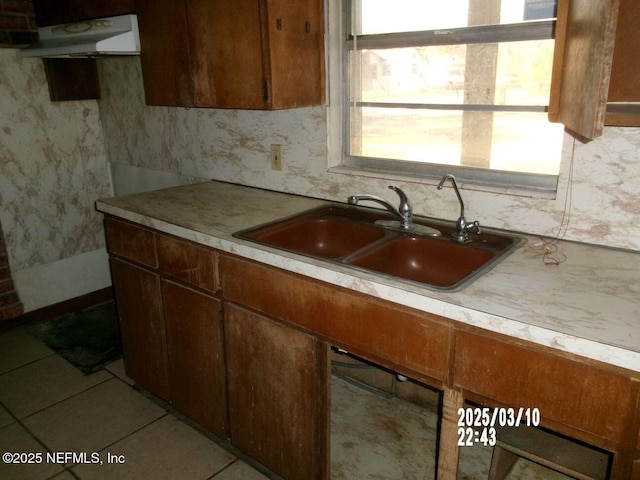 kitchen featuring tasteful backsplash, under cabinet range hood, light countertops, light tile patterned floors, and a sink