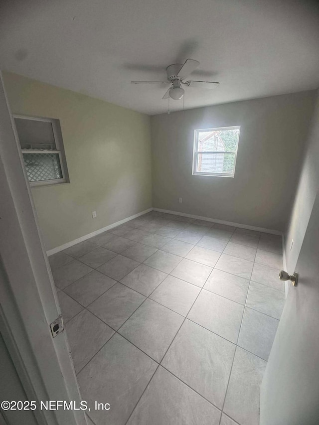 empty room featuring tile patterned floors, a ceiling fan, and baseboards