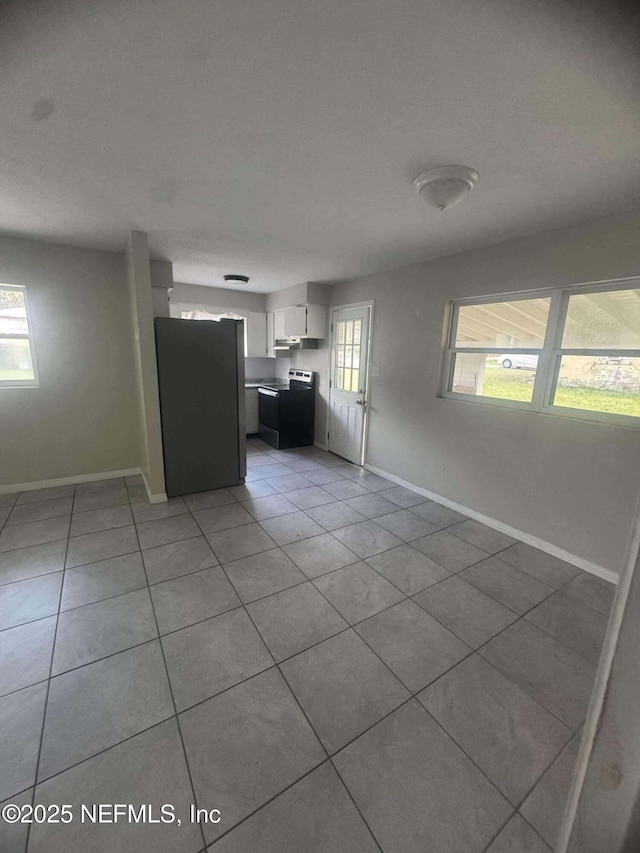 kitchen featuring baseboards, light tile patterned floors, range with electric stovetop, freestanding refrigerator, and white cabinetry