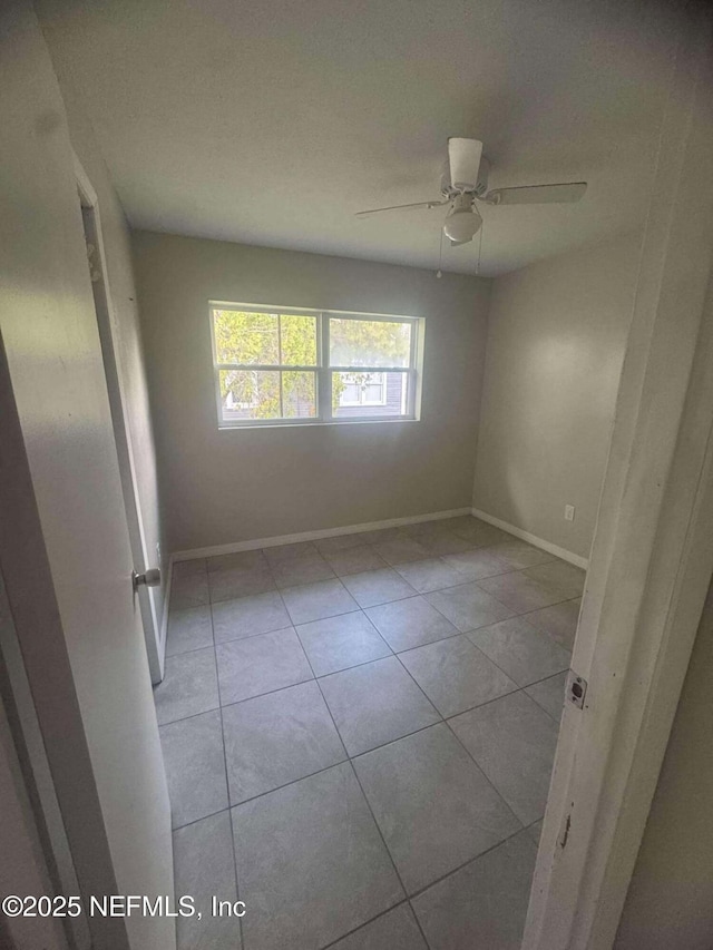 empty room with tile patterned flooring, ceiling fan, and baseboards