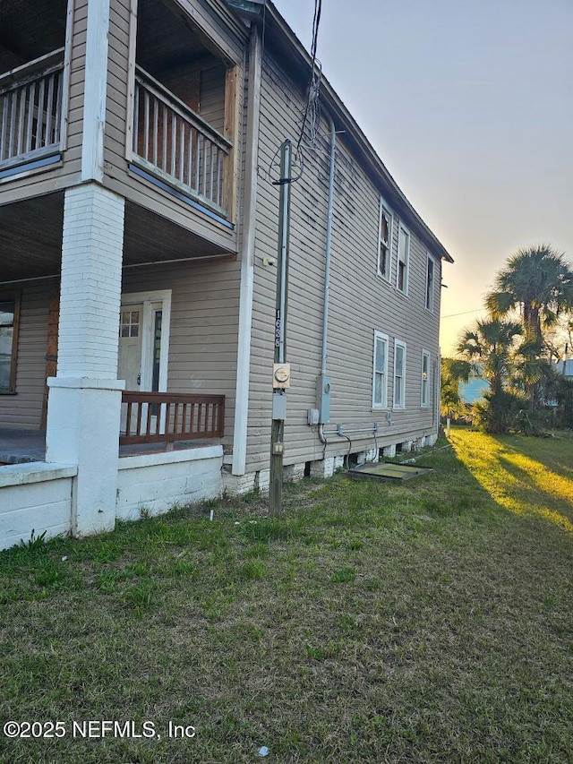 property exterior at dusk with a balcony, a porch, and a yard