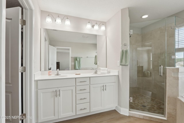 full bath featuring a shower stall, wood finished floors, double vanity, and a sink