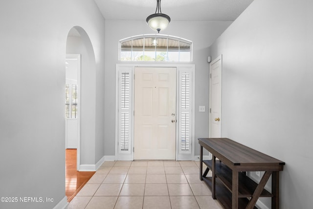 foyer entrance with light tile patterned floors, baseboards, and arched walkways