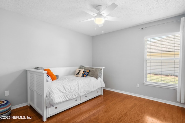 bedroom with a ceiling fan, wood finished floors, baseboards, and a textured ceiling