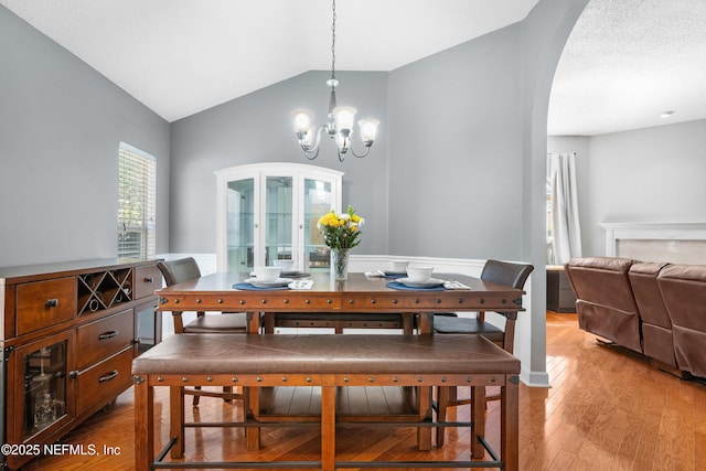 dining room featuring lofted ceiling, a notable chandelier, arched walkways, and light wood finished floors