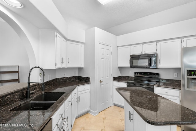 kitchen with black appliances, a sink, dark stone countertops, white cabinetry, and light tile patterned floors