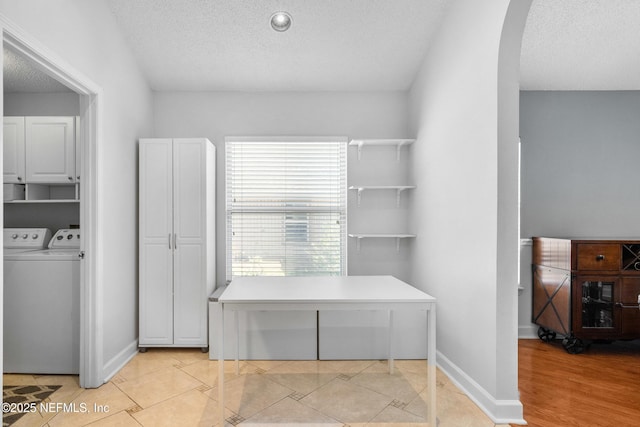 laundry room with light tile patterned floors, baseboards, arched walkways, a textured ceiling, and washer and clothes dryer