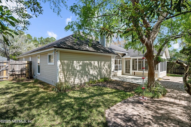 back of house with fence, a lawn, a chimney, a sunroom, and a patio area