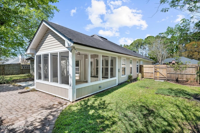 back of house with a gate, a fenced backyard, a sunroom, a shingled roof, and a lawn