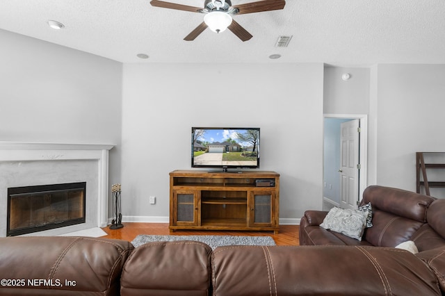 living area featuring visible vents, baseboards, ceiling fan, wood finished floors, and a textured ceiling