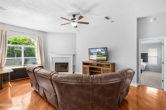 living area featuring light wood finished floors, visible vents, a ceiling fan, and a glass covered fireplace