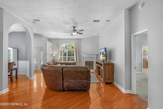 living area featuring visible vents, arched walkways, ceiling fan, and light wood finished floors